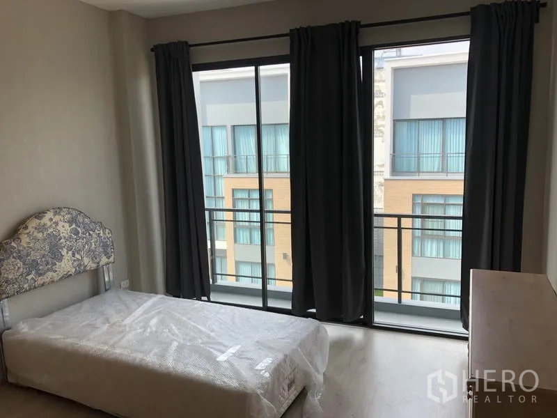Townhouse for rent in Suan Luang, Bangkok - Bedroom with sliding glass doors to a balcony and dark curtains.