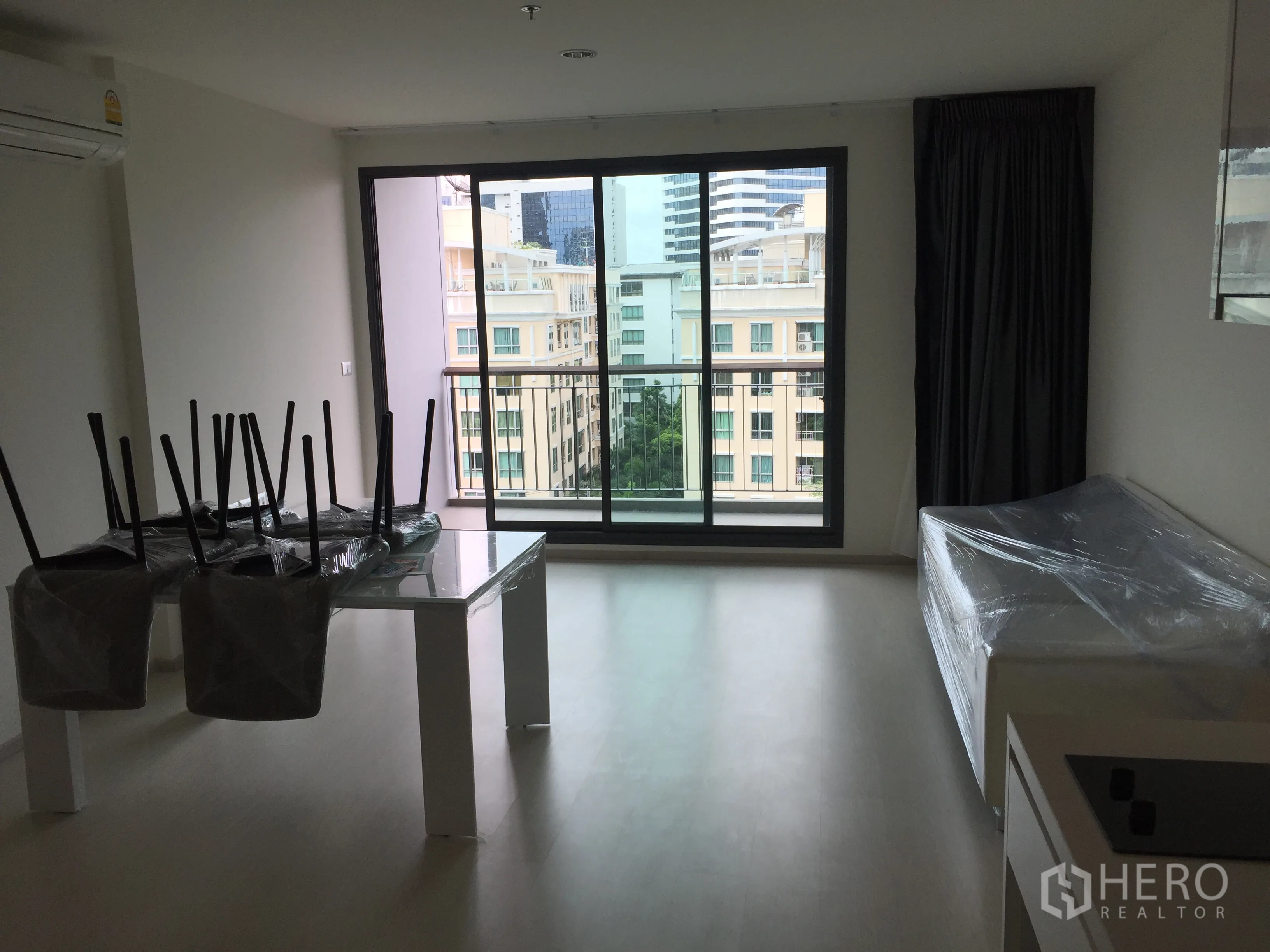Condominium for rent in Khlong Toei, Bangkok - Bright living room with floor-to-ceiling sliding doors opening to a balcony with city views.