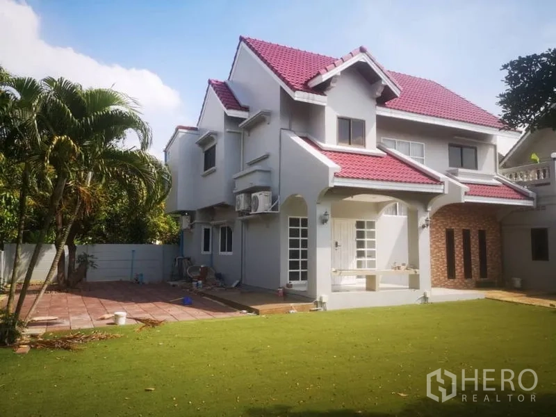 Detached House for rent in Samut Prakan - Two‑storey house exterior with red tile roof and expansive green lawn.