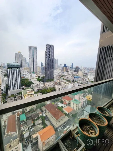 Condominium for rent in Bang Rak, Bangkok - High‑floor balcony with glass railing overlooking Bangkok city skyline and dense urban neighborhood.