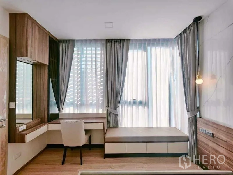 Condominium for rent in Ratchathewi, Bangkok - Bright corner with built-in desk and vanity beside large curtained windows.