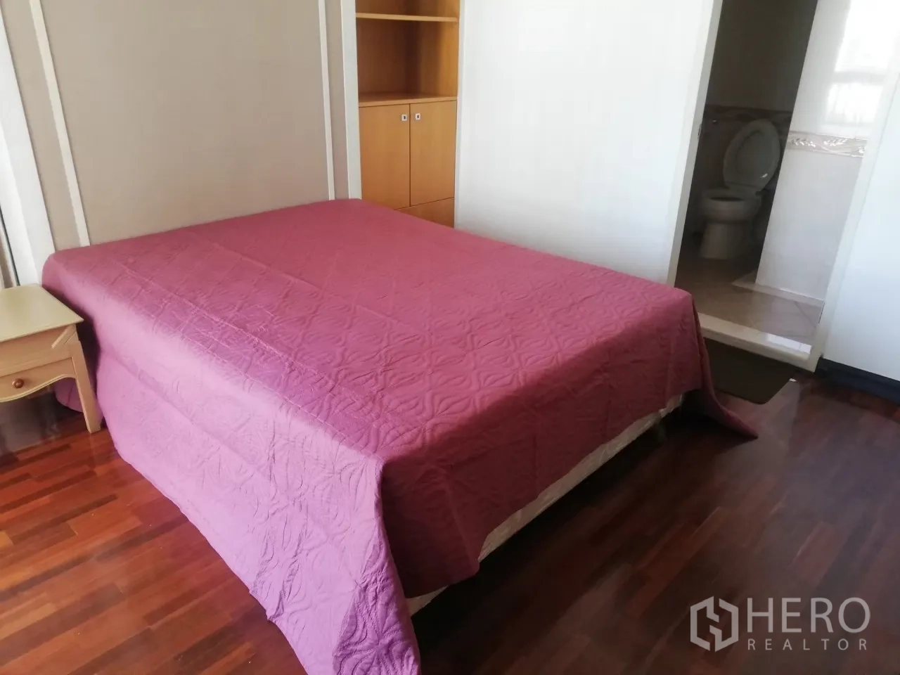 Condominium for rent in Phaya Thai, Bangkok - Bedroom with pink bedspread, built-in shelves and an en-suite bathroom entrance.