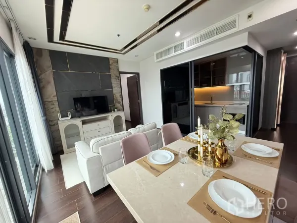 Condominium for rent in Watthana, Bangkok - Open living and dining area with sofa, TV wall, and kitchen behind sliding glass.