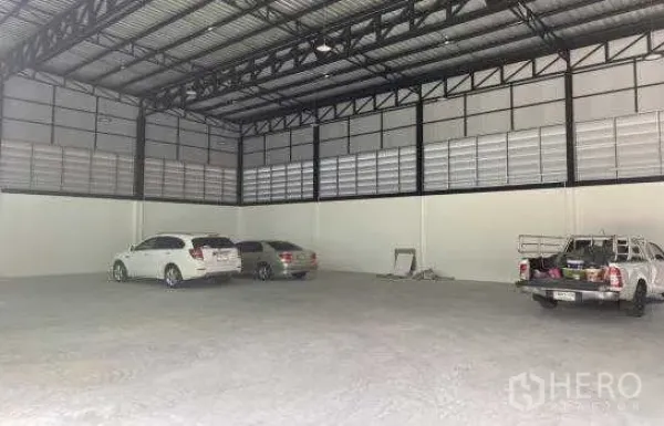Warehouse for rent in Prawet, Bangkok - Spacious warehouse interior with high steel truss roof and open concrete floor, suitable for vehicle parking and storage.