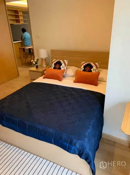 公寓 出租在Watthana, Bangkok - 主卧以暖色调为主，海军蓝床品、木质床架与柔和灯光。