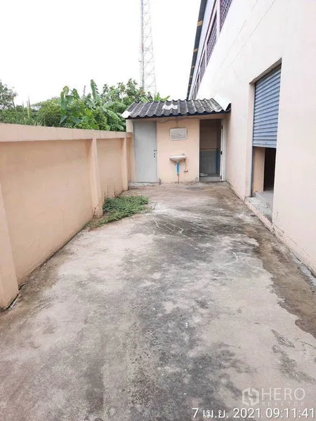 Factory for rent in Bang Bua Thong, Nonthaburi - Concrete side yard with utility sink, boundary wall and access doors.