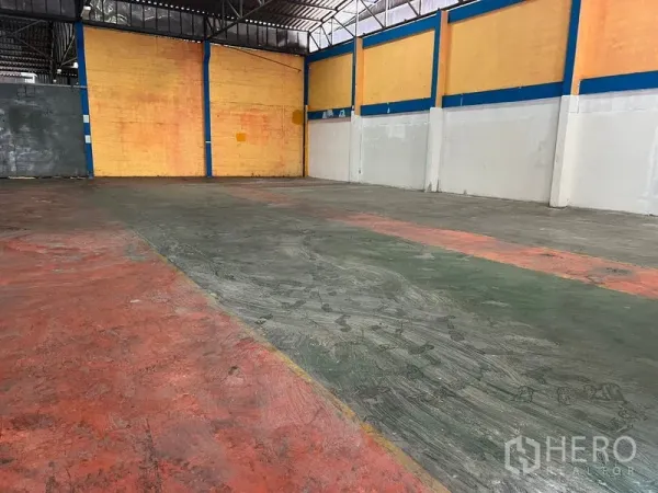 Warehouse for rent in Mueang Samut Prakan, Samut Prakan - Open storage bay with concrete floor, yellow wall panels, blue steel columns and ample headroom.