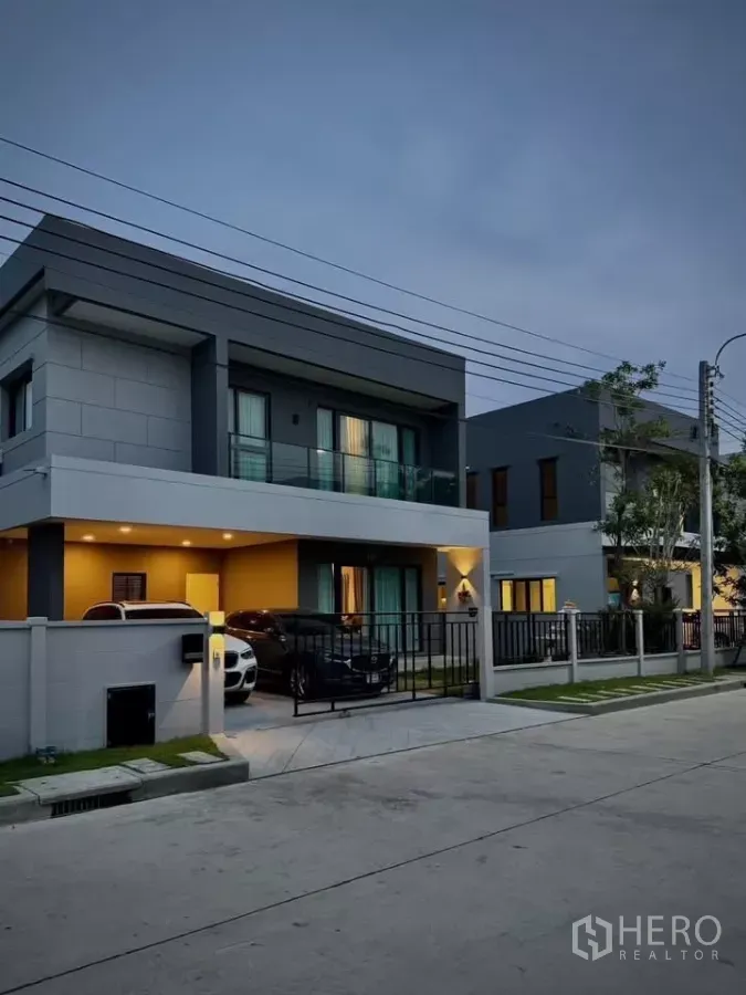 独立式住宅 出租在Bang Phli, Samut Prakan - 两层现代独栋住宅，带阳台与带大门的双车位车棚，傍晚外观。