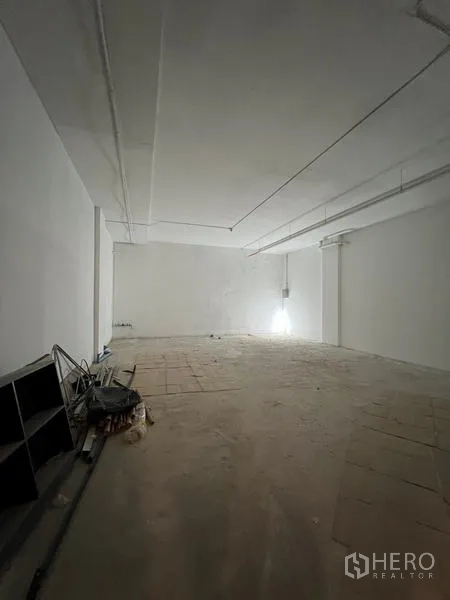 Retail Space for rent - Long rectangular shop interior with high ceiling, unfinished flooring and utility points along the side wall.