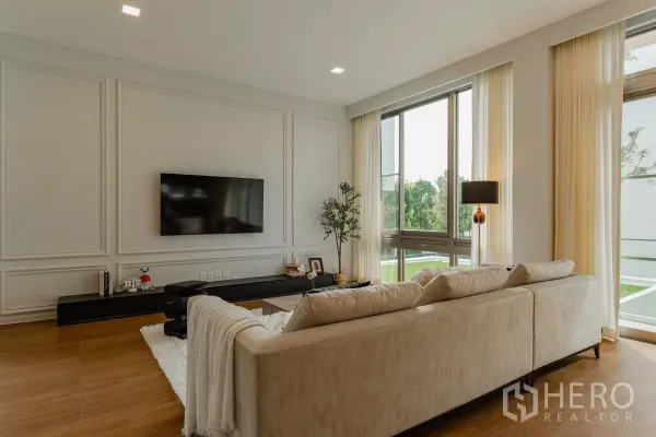 Detached House for rent in Saphan Sung, Bangkok - Spacious lounge with large windows and wall-mounted TV facing green lawn.