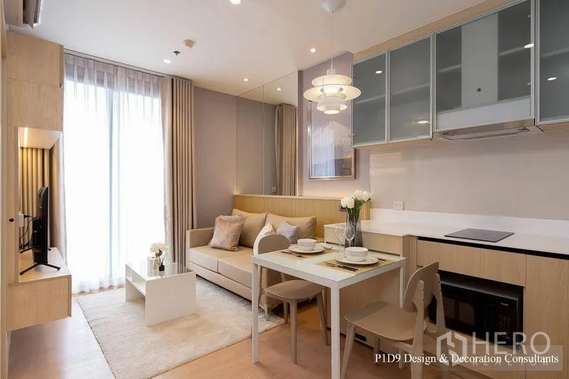 公寓 出租在Watthana, Bangkok - 客厅带阳台玻璃门与镜面墙，舒适沙发，L形厨房连餐桌。