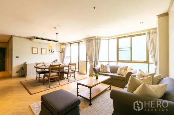 Apartment for rent in Khlong Toei, Bangkok - Bright open-plan living and dining area with large windows, two sofas, and a wooden table near BTS Ekkamai.
