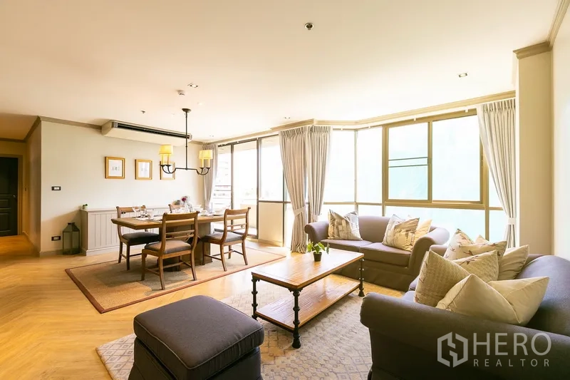Apartment for rent in Khlong Toei, Bangkok - Bright open-plan living and dining area with large windows, two sofas, and a wooden table near BTS Ekkamai.