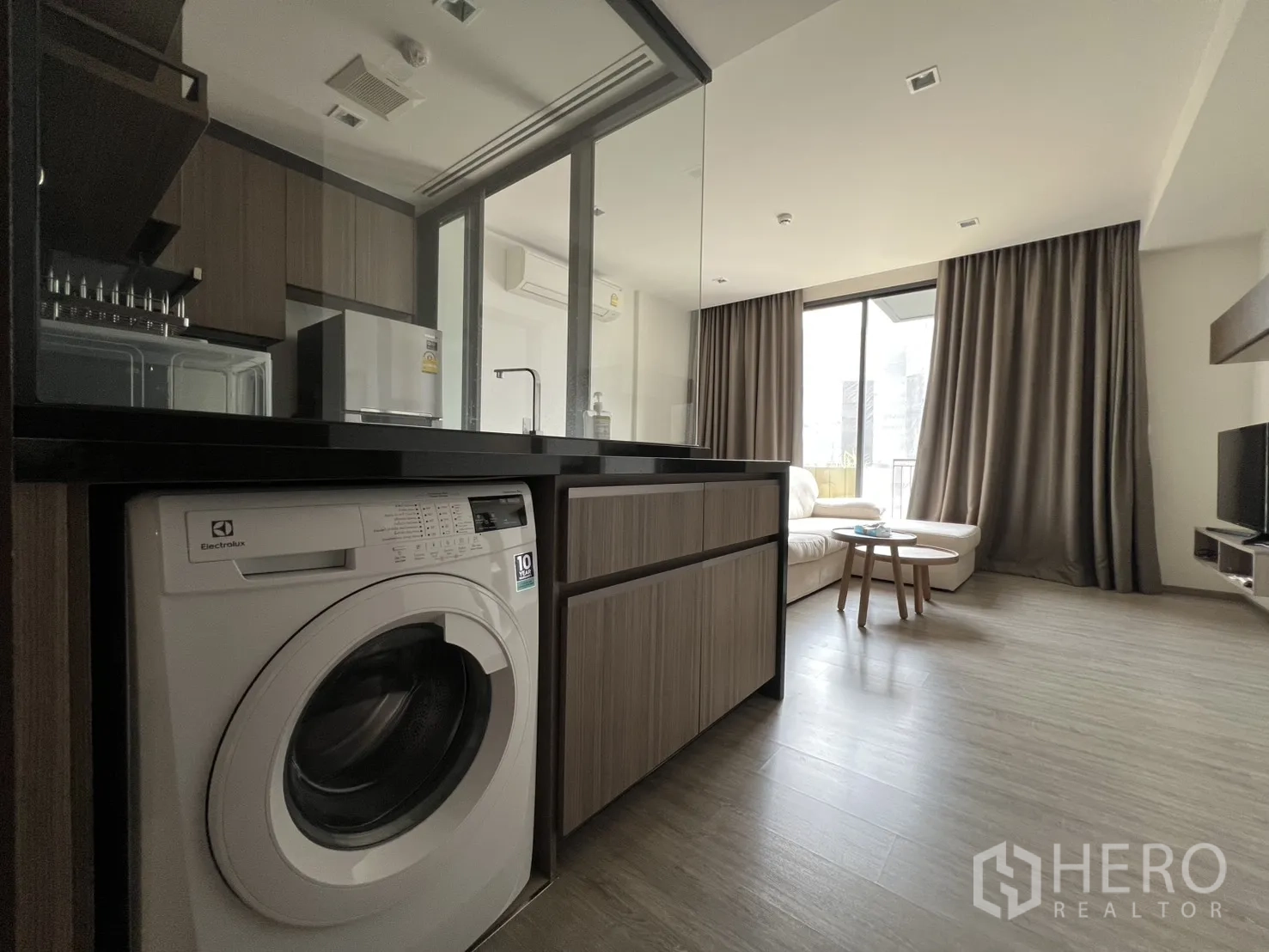 คอนโด for rent in Watthana, Bangkok - ห้องนั่งเล่นแบบโอเพ่นพร้อมโซฟา L-shape ครัวกั้นกระจก และเครื่องซักผ้าในตู้บิลต์อิน.
