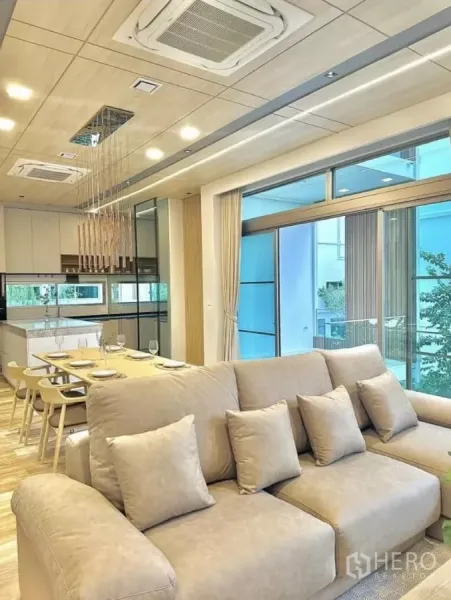Detached House for rent in Saphan Sung, Bangkok - Living room view toward kitchen with beige sectional sofa, expansive glazing and built‑in cabinetry.