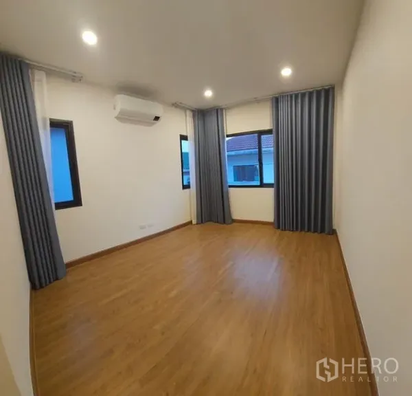 Detached House for rent in Saphan Sung, Bangkok - Spacious bedroom with wood flooring, multiple windows, curtains and air conditioning.