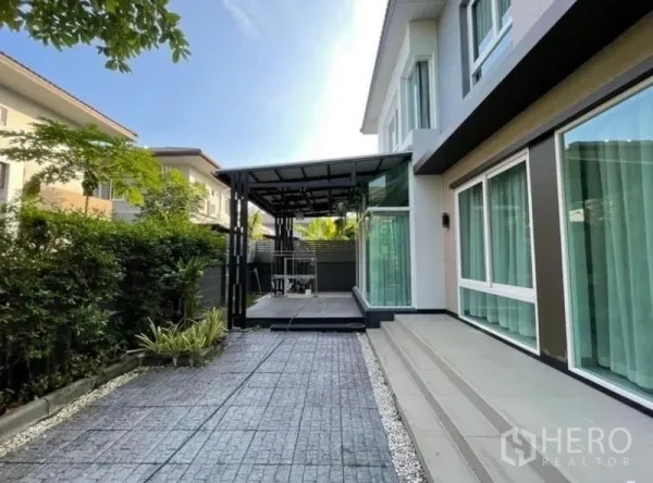 Detached House for rent or sale in Bang Phli, Samut Prakan - Side yard with covered terrace, glass sunroom and paved walkway bordered by green hedges.