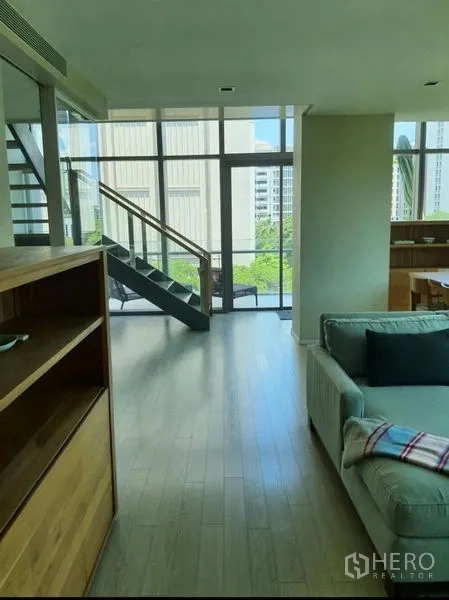 公寓 出租或出售在Watthana, Bangkok - 阁楼风客厅，挑高落地窗、浅色木地板与金属玻璃楼梯