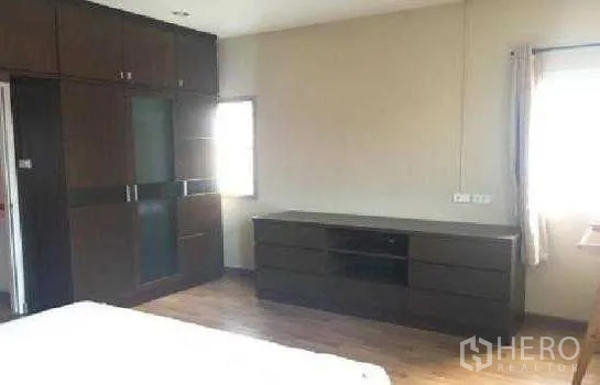Home Office for rent in Lat Phrao, Bangkok - Master bedroom with built-in wardrobes, long dresser, wood floors and a window.