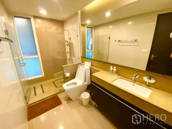 公寓 出租在Ratchathewi, Bangkok - 明亮浴室，玻璃淋浴间、长台面洗手台与大镜面。