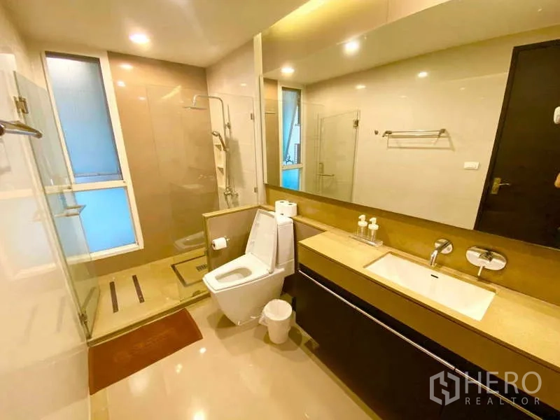 公寓 出租在Ratchathewi, Bangkok - 明亮浴室，玻璃淋浴间、长台面洗手台与大镜面。