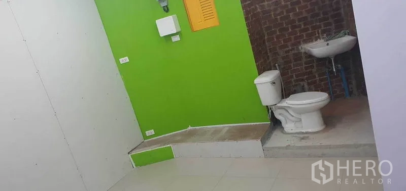 Retail Space for rent in Khlong Toei, Bangkok - Small bathroom with toilet, wall-mounted sink, bright green wall and exposed brick.