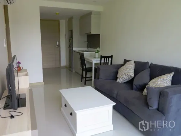 Condominium for rent or sale in Watthana, Bangkok - Open-plan living area with compact kitchenette, dining counter, and grey sofa in a 1-bedroom Ekkamai condominium.