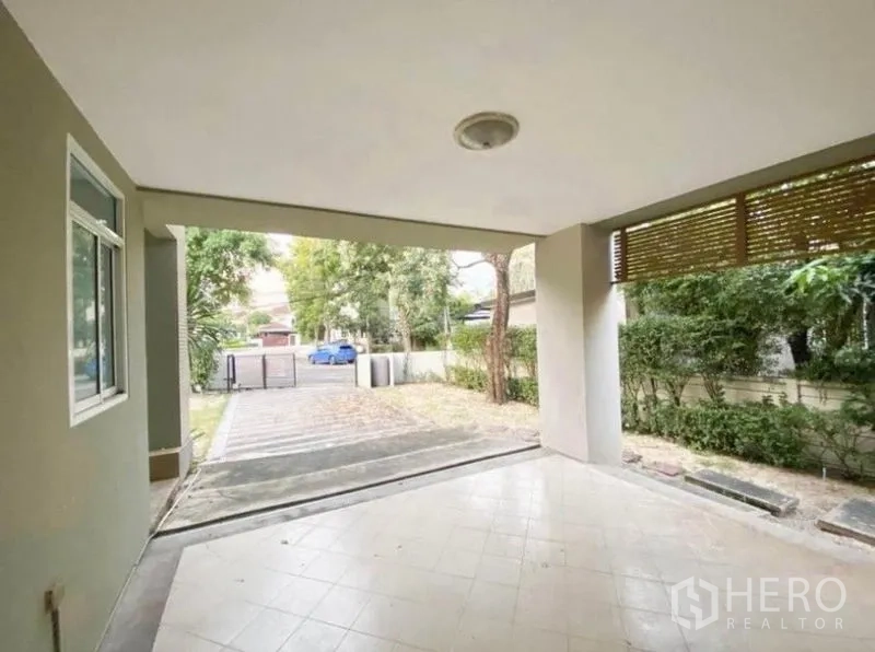 Detached House for sale in Saphan Sung, Bangkok - Covered carport and terrace facing the driveway with hedges and trees along the boundary.