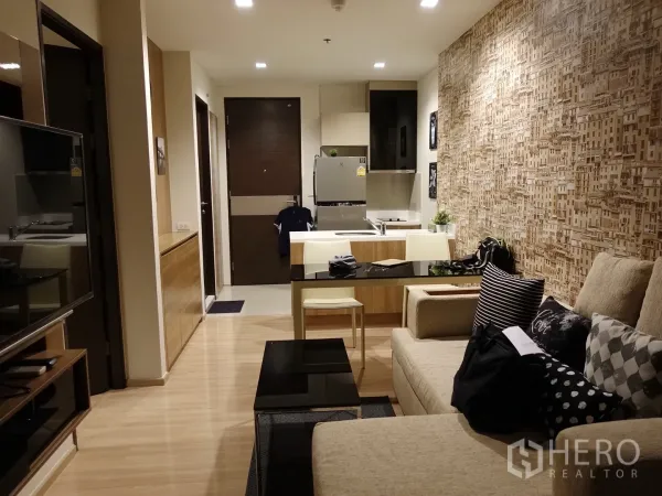 Condominium for rent in Sathon, Bangkok - Open-plan living area facing the kitchen island, TV wall, beige sofa and warm wood flooring.