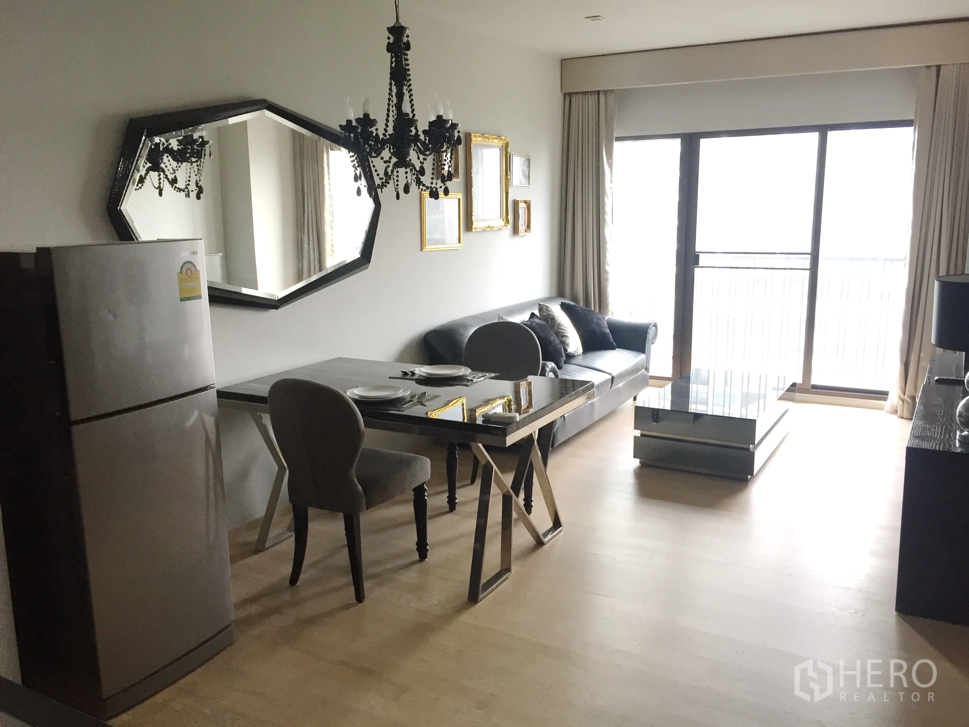 Condominium for rent in Bangkok - Bright living and dining area with chandelier, large wall mirror, sofa, dining table and sliding doors to the balcony.