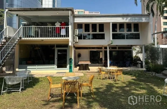 零售空间 for rent in Khlong Toei, Bangkok - 两层建筑带玻璃立面与阳台，前方草坪摆放多组户外桌椅。