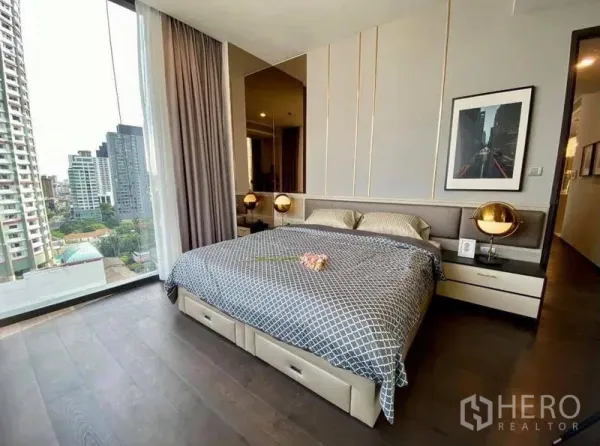 公寓 出租在Watthana, Bangkok - 主卧配特大床与床头灯，落地窗可赏曼谷城市景观。