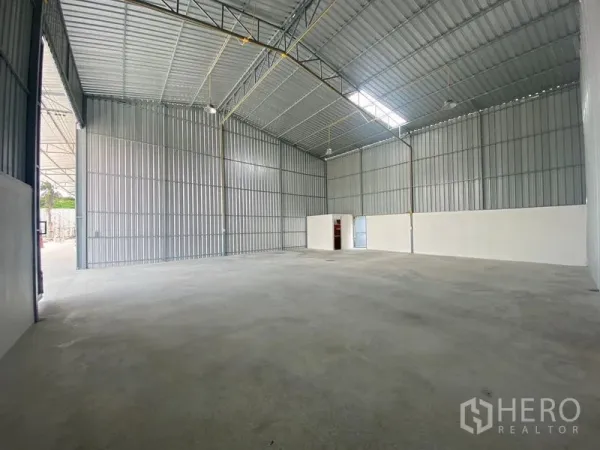 Warehouse for rent in Mueang Nonthaburi, Nonthaburi - Wide open warehouse floor with metal sheet walls, bright lighting, and a small partitioned room at the back.