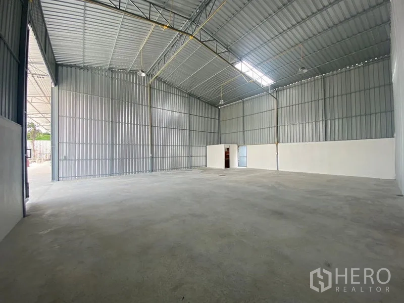 Warehouse for rent in Mueang Nonthaburi, Nonthaburi - Wide open warehouse floor with metal sheet walls, bright lighting, and a small partitioned room at the back.