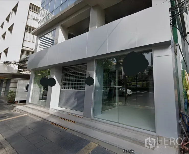 零售空间 出租在Bang Rak, Bangkok - 是隆区现代商业楼外立面，带大面积玻璃橱窗、卷闸门与街道台阶入口。