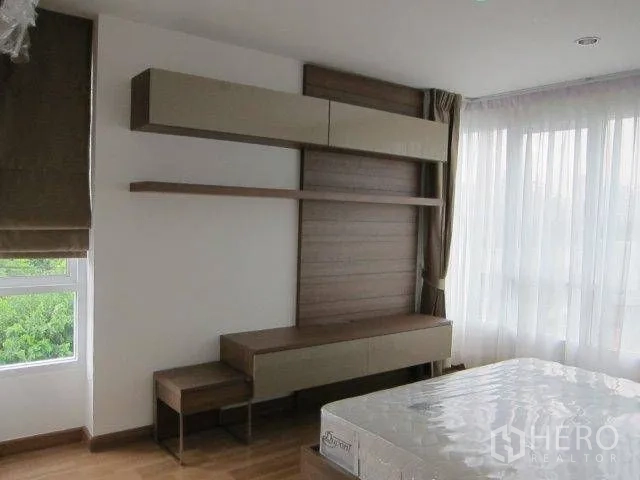 Condominium for rent in Khlong Toei, Bangkok - Bedroom with wide windows, wood flooring, and wall-mounted storage and shelves.