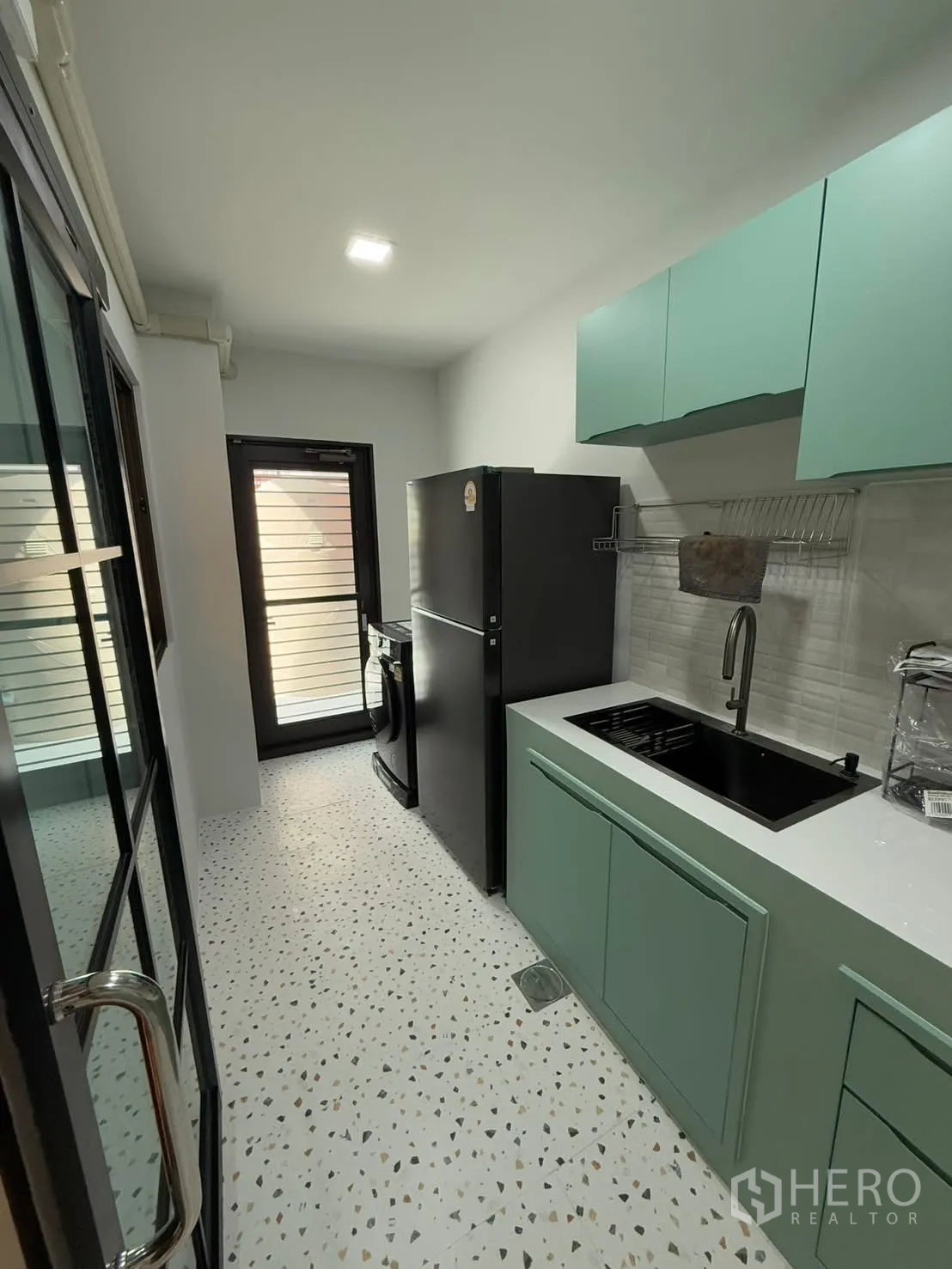 联排别墅 for rent in Bang Phli, Samut Prakan - 厨房另一角度，带大冰箱、水槽、吊柜及通往后阳台的门。