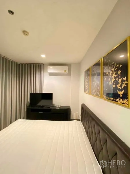 Condominium for rent in Khlong Toei, Bangkok - Bedroom view with bed, curtains, TV cabinet, air conditioner and gold-trim wall art.