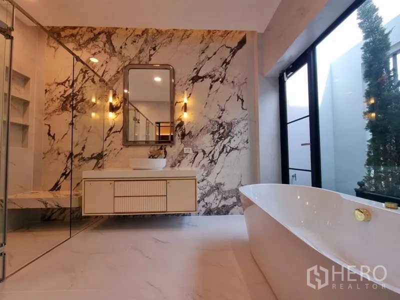Detached House for rent in Saphan Sung, Bangkok - Luxury bathroom with freestanding bathtub, marble feature wall, glass shower, and large window.
