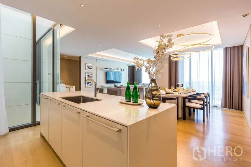 Condominium for sale in Pathum Wan, Bangkok - Kitchen island overlooking dining area with statement halo lights and full-height windows