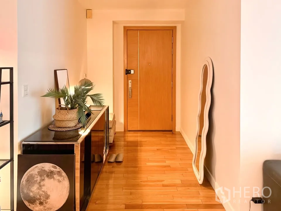 Condominium for rent or sale in Khlong Toei, Bangkok - Entrance hallway with a wooden door, console table, decorative mirror, and warm wood flooring.