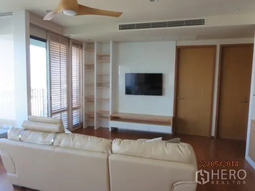 Condominium for rent in Bang Rak, Bangkok - Living room with a cream sectional sofa, wall-mounted TV and built-in shelves.