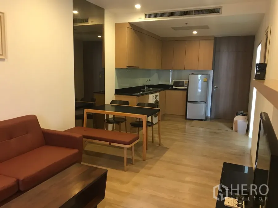 Condominium for rent in Bangkok - Open-plan living room with sofa, dining set, and fitted corner kitchen with appliances in a Bangkok condo.