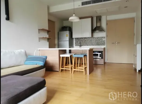 Condominium for rent in Khlong Toei, Bangkok - Open-plan living room with island kitchen, mosaic backsplash, and wood flooring.