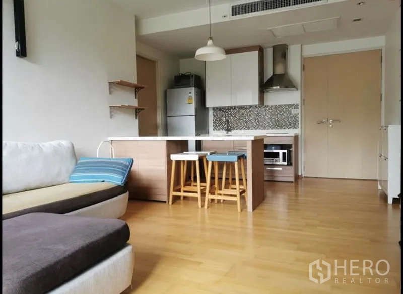 Condominium for rent in Khlong Toei, Bangkok - Open-plan living room with island kitchen, mosaic backsplash, and wood flooring.