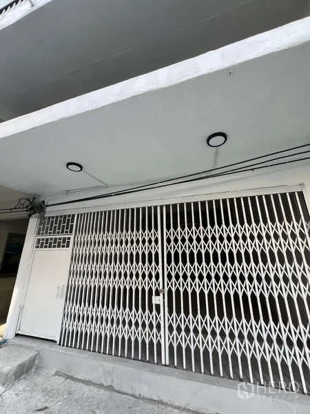 Shophouse for rent in Watthana, Bangkok - White shophouse facade with folding metal security gate and canopy lighting.