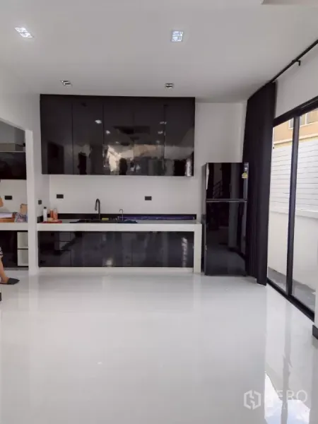 Detached House for rent in Wang Thonglang, Bangkok - Modern white kitchen with glossy black cabinets, sink, and sliding glass doors.