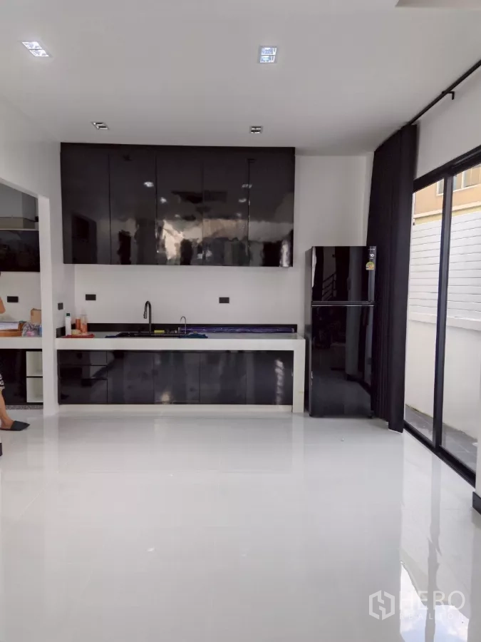 Detached House for rent in Wang Thonglang, Bangkok - Modern white kitchen with glossy black cabinets, sink, and sliding glass doors.