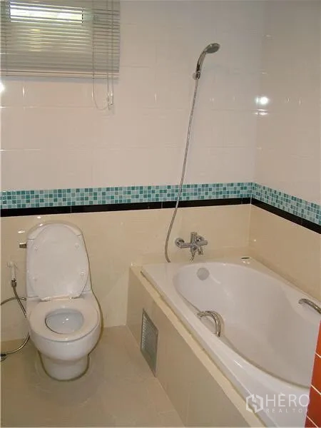 Condominium for rent in Khlong Toei, Bangkok - Clean bathroom featuring a soaking bathtub, handheld shower, toilet, and mosaic tile accents.