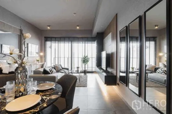 Condominium for rent in Watthana, Bangkok - Bright living room with large glazing, wall-mounted TV, mirrored feature wall and balcony access.